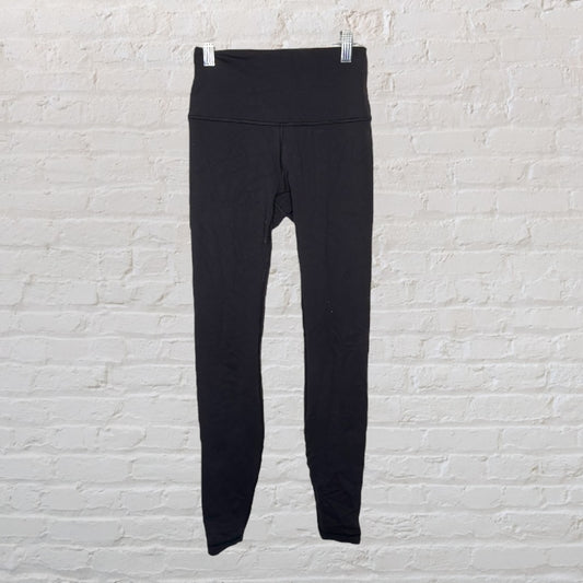 Black high-waisted women's leggings hanging against a white brick wall.