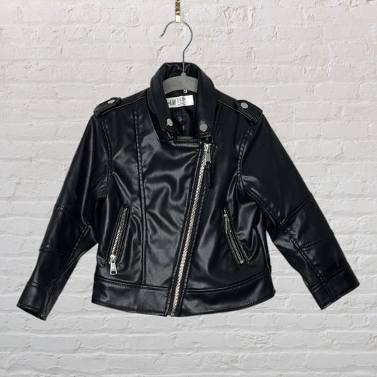 Black faux leather kids biker jacket with asymmetric zipper and silver hardware, by H&M, hanging on a hook.