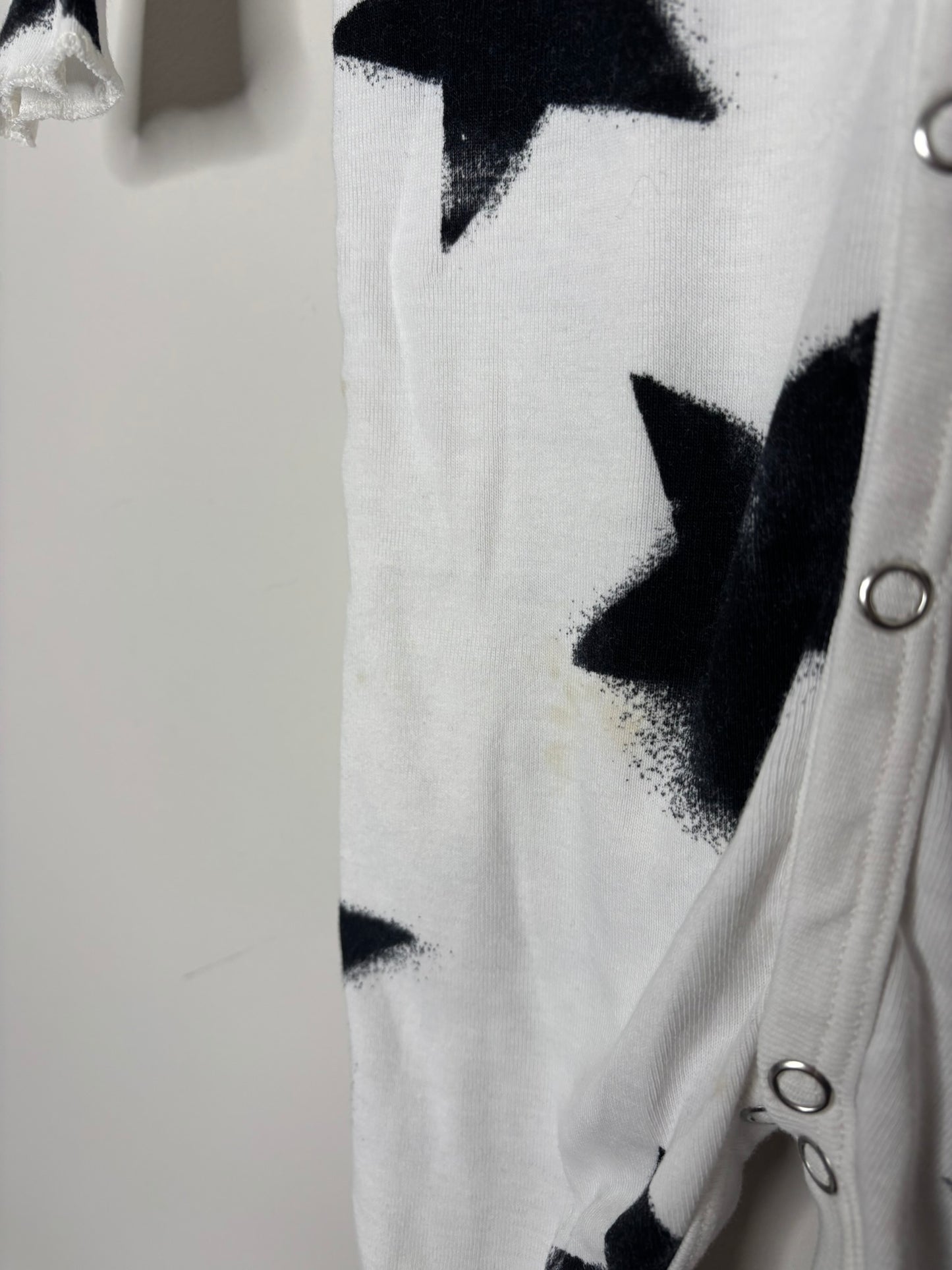 White baby onesie with black star print, featuring snap buttons down the front, hanging on a hanger against a brick wall.