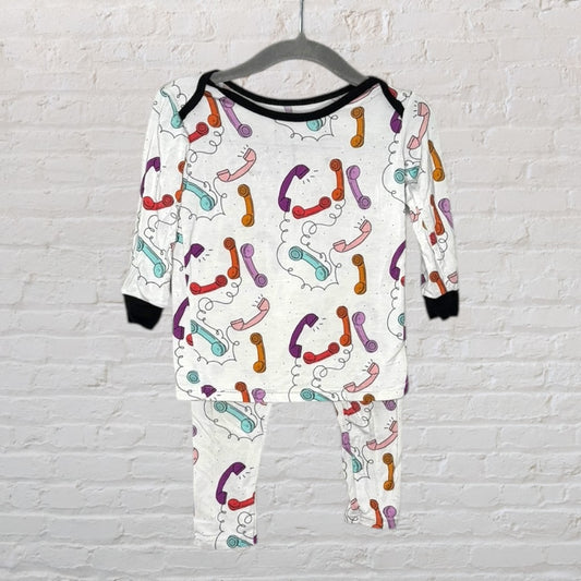 Unisex white pajama set featuring a colorful retro phone print, displayed on a hanger against a brick wall.