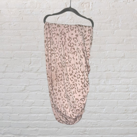 Pink and brown leopard print infinity scarf hanging on a black hanger against a white brick wall.