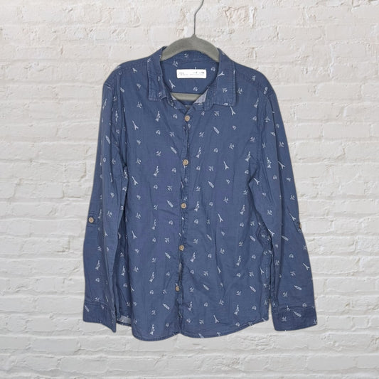 Men's blue button-up shirt with small white patterns, hanging on a hanger against a white brick wall.