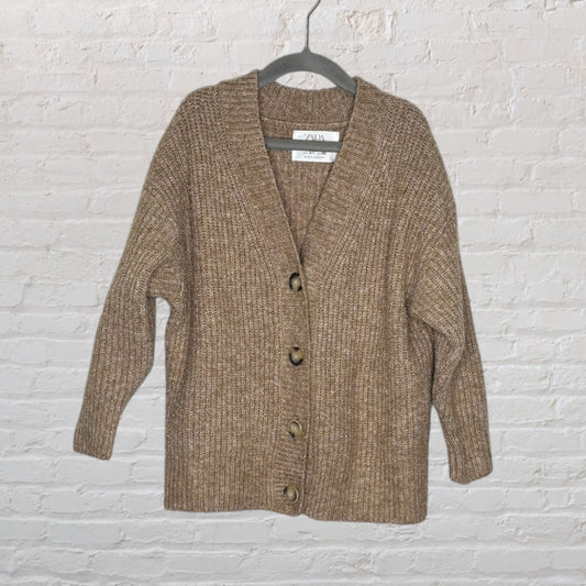 Brown chunky knit cardigan with large buttons from Zara, displayed on a hanger against a white brick wall.