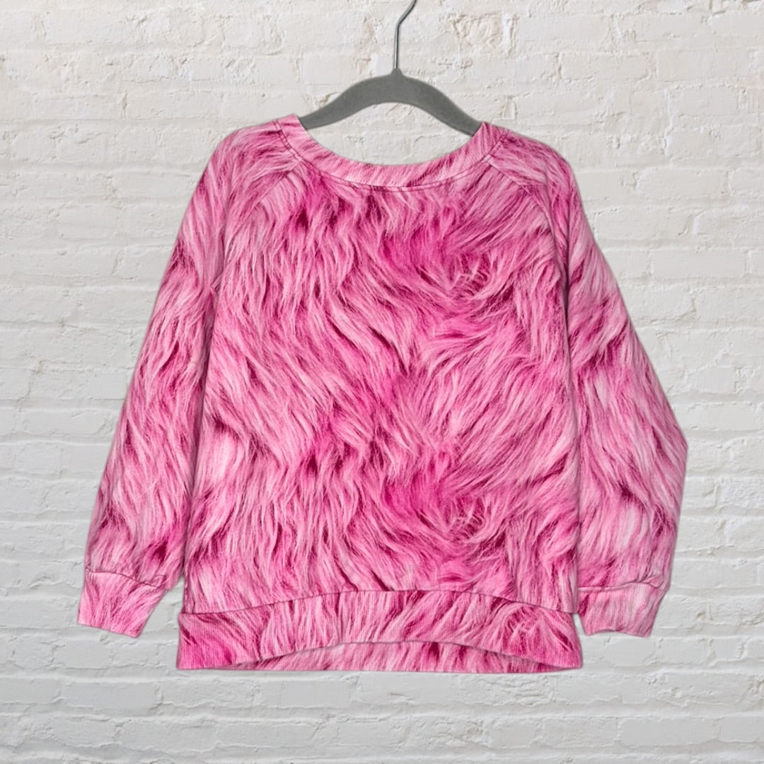 Pink sweatshirt with a faux fur texture print hanging on a hanger against a brick wall.