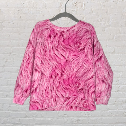 Pink sweatshirt with a faux fur texture print hanging on a hanger against a brick wall.