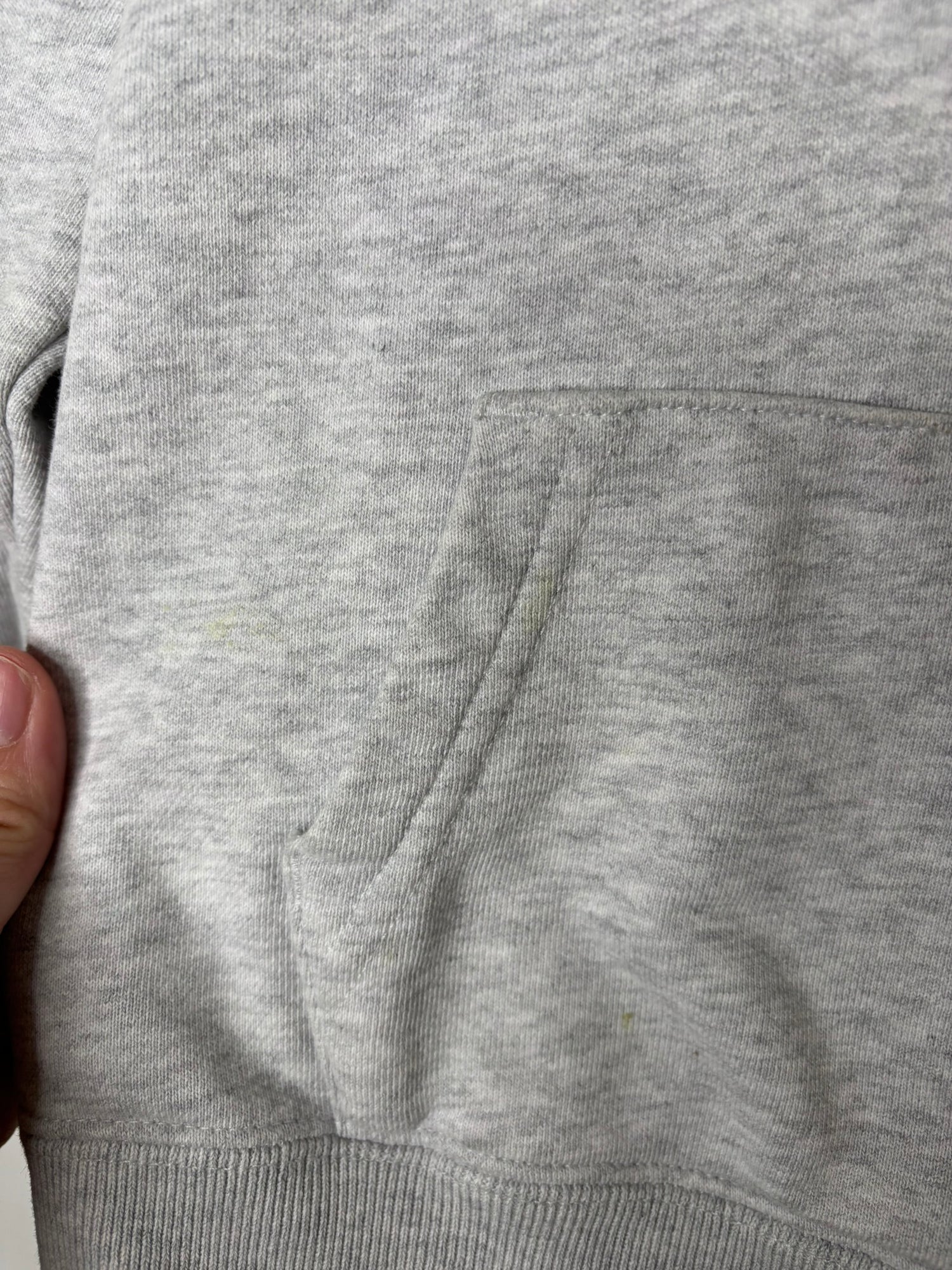 Grey hoodie featuring a small embroidered owl logo on the chest, displayed against a white brick wall.