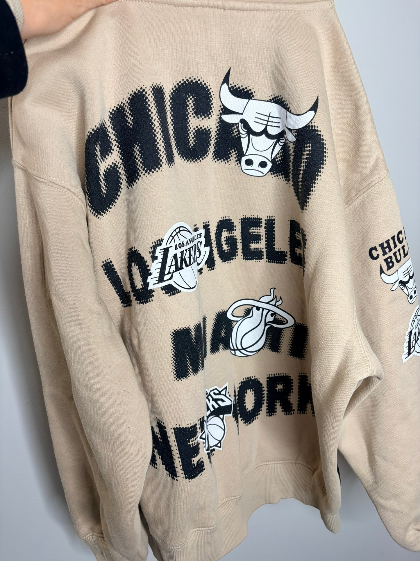 Beige NBA hoodie featuring team logos on the sleeve and NBA logo on the front.