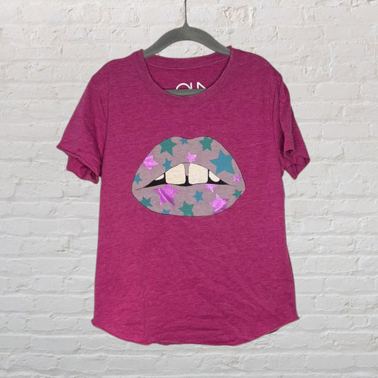 Purple t-shirt with a graphic of lips adorned with stars in various colors, hanging on a hanger against a white brick background.