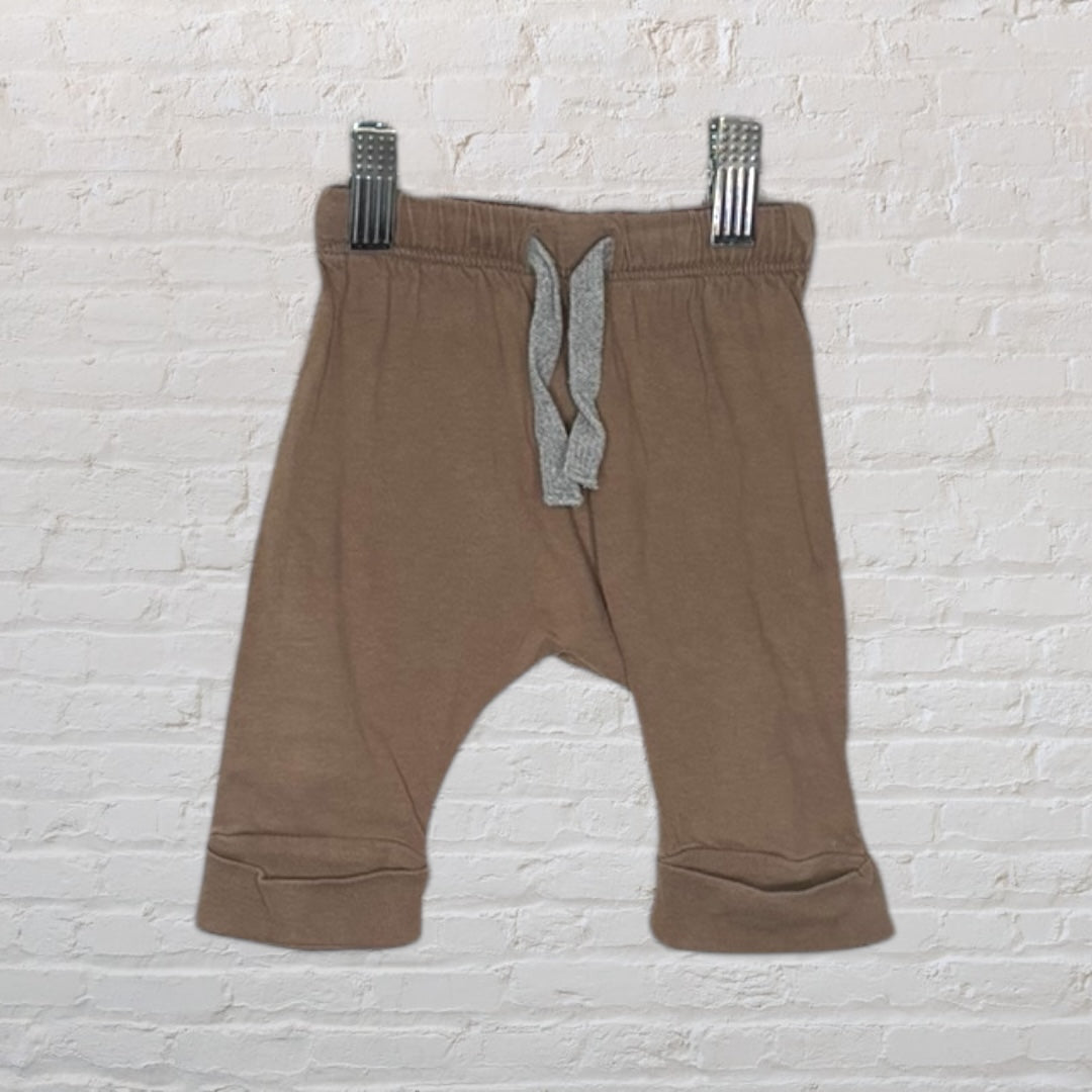 Brown baby jogger pants with an elastic waistband and grey drawstring, clipped against a white brick background.