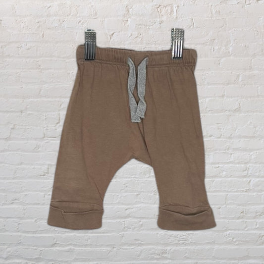 Brown baby jogger pants with an elastic waistband and grey drawstring, clipped against a white brick background.