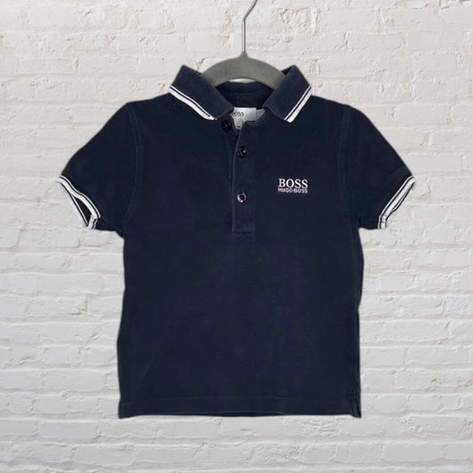 Navy blue Hugo Boss polo shirt with white logo and striped collar, displayed on a hanger.