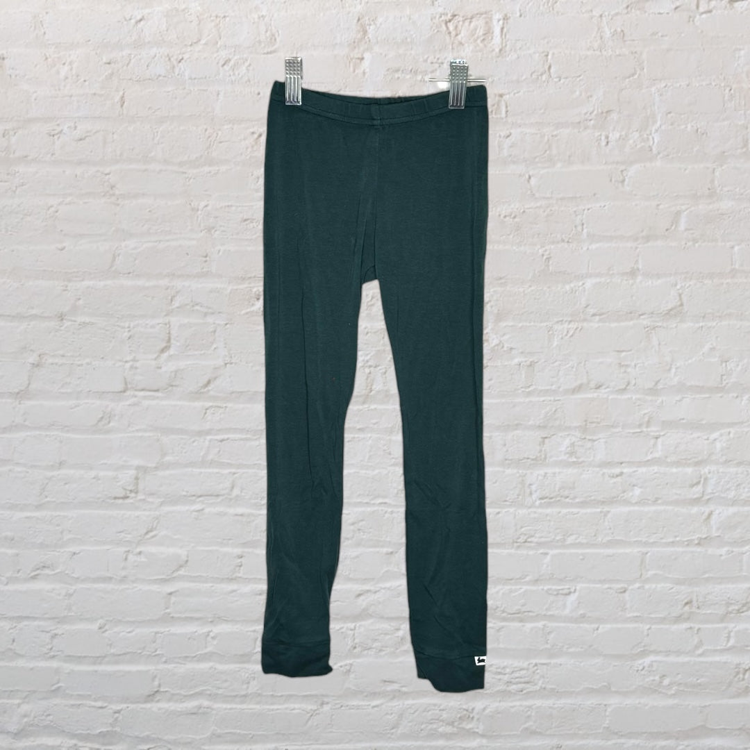 Dark green leggings hanging on a background clip against a white brick wall.