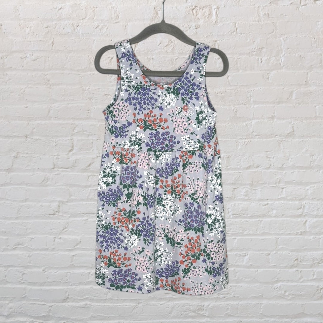 Sleeveless dress with a floral pattern in lavender, white, pink, and green, hanging on a dark hanger against a brick wall.