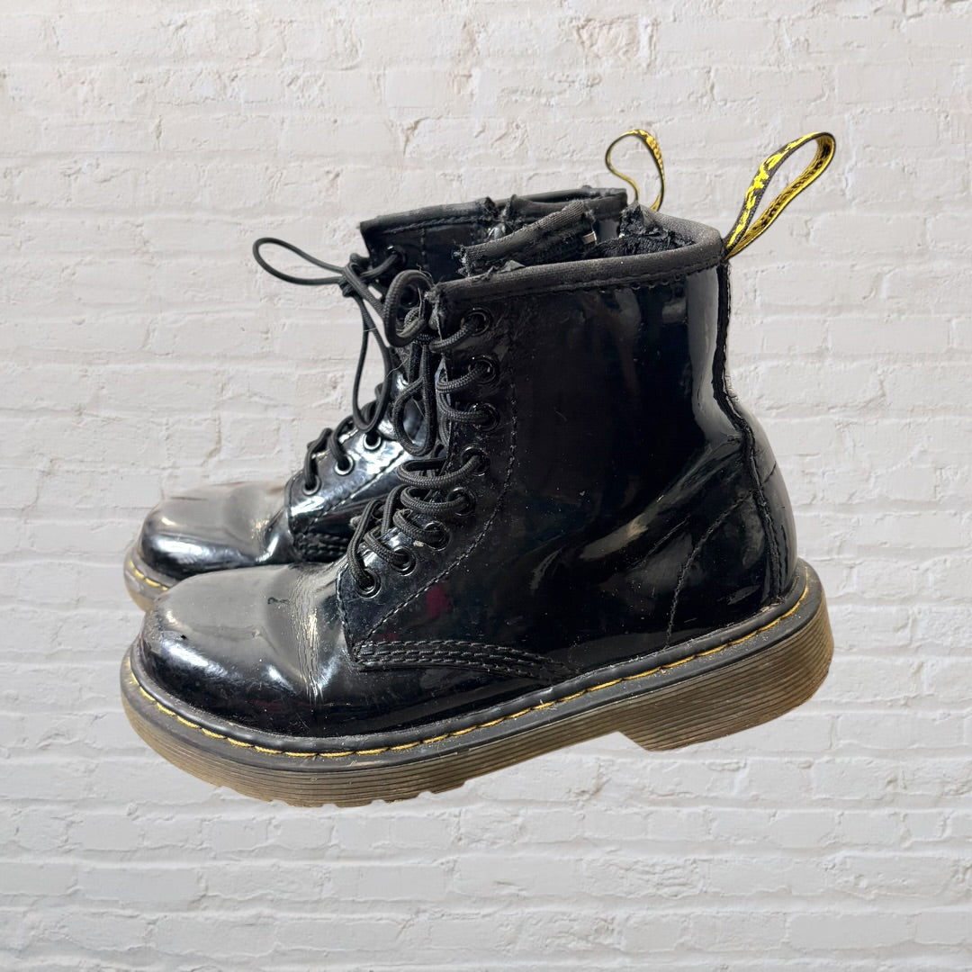 Shiny black patent leather lace-up boots with yellow stitching and pull tabs, showing visible wear.