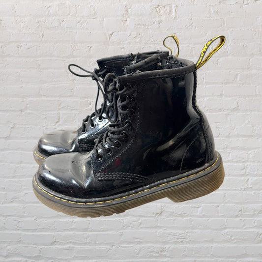 Shiny black patent leather lace-up boots with yellow stitching and pull tabs, showing visible wear.
