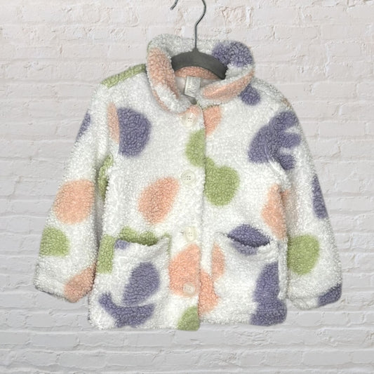 Cozy sherpa jacket with polka dots in pastel colors, features buttons and pockets, hanging on a gray hanger.