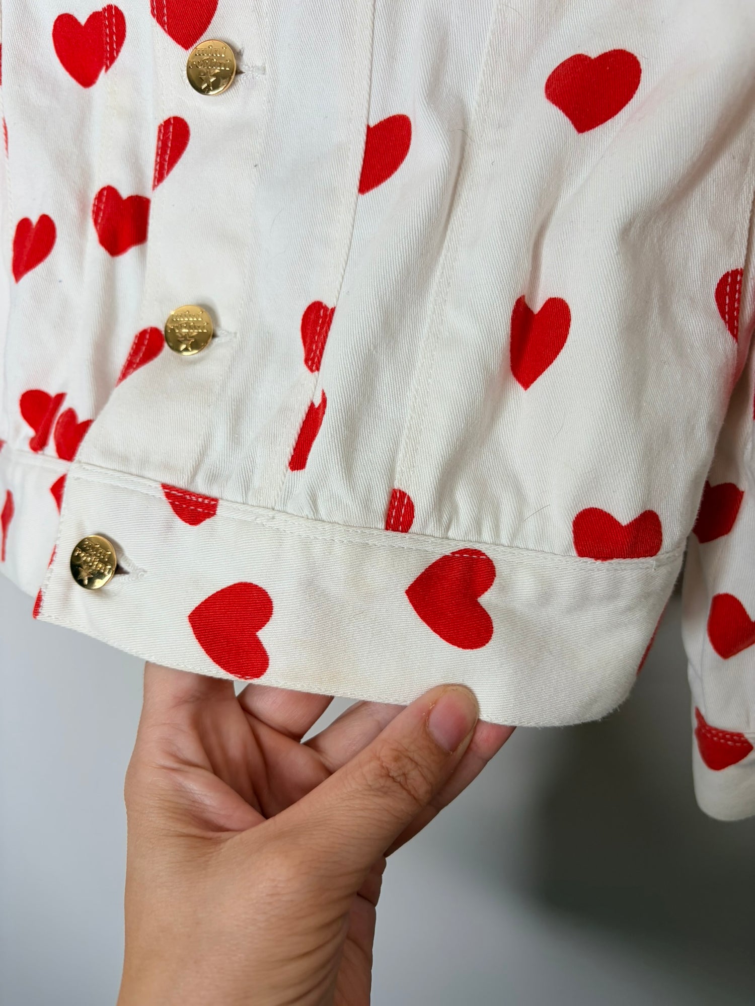 Mini Rodini white denim jacket with red heart prints and gold buttons.