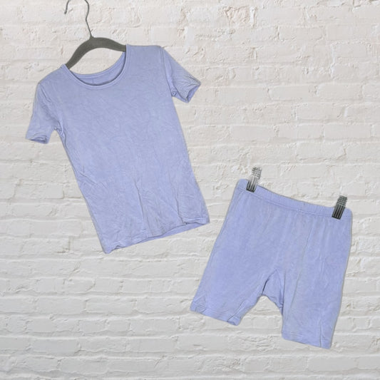 Light purple short-sleeve loungewear set with a T-shirt and shorts hanging against a white brick wall.