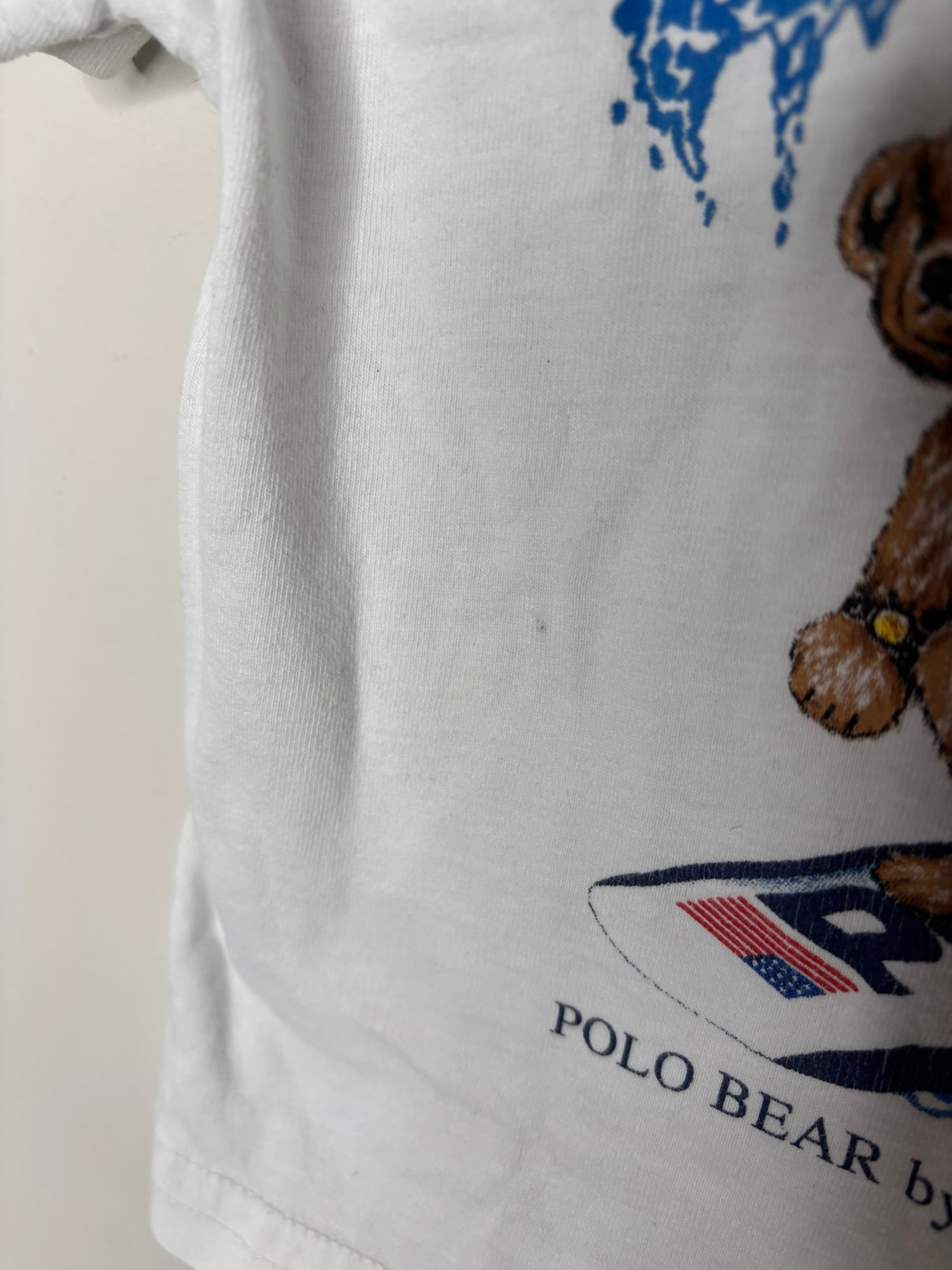White Ralph Lauren T-shirt with a surfing Polo Bear graphic, featuring button details on the shoulder.