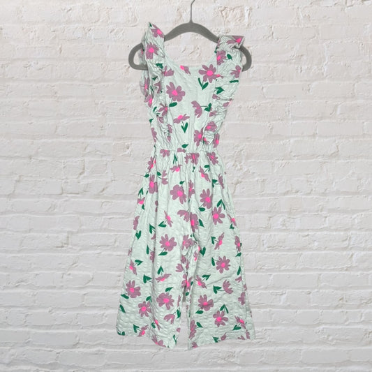 White sleeveless dress with pink floral print and ruffled details, hanging on a hanger.