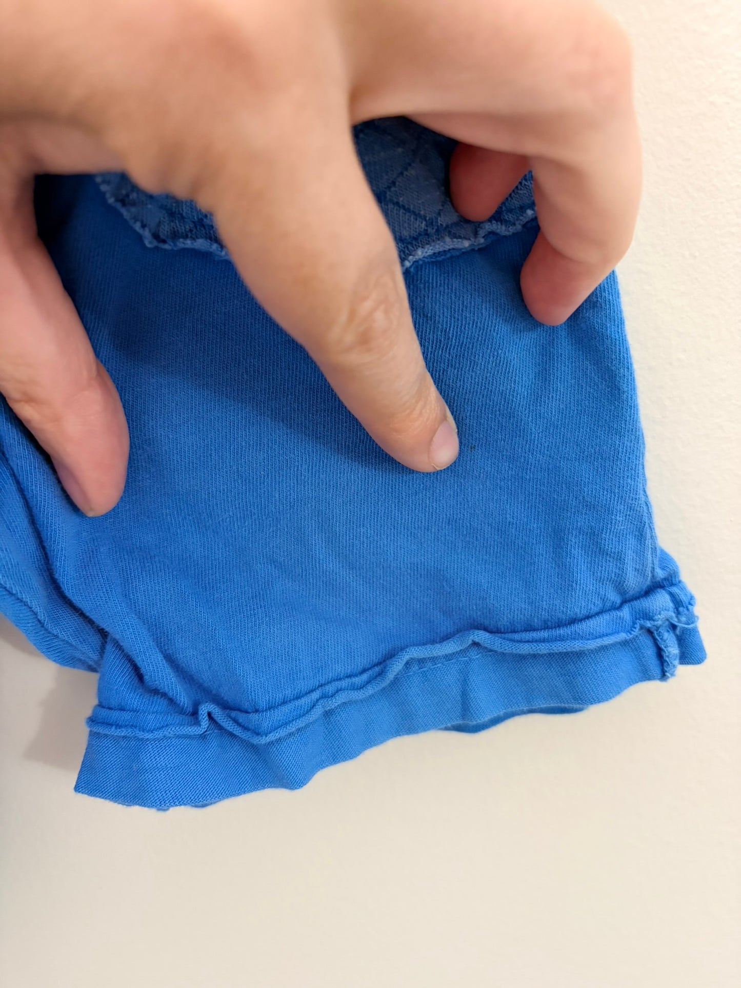 Blue kids shorts with quilted pockets, displayed on a hanger against a white brick background.