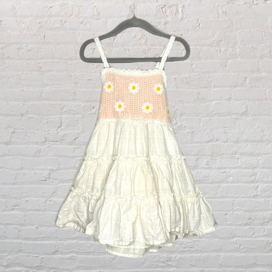 Cream and peach sundress with crochet top and daisy embellishments, hanging on a black hanger.