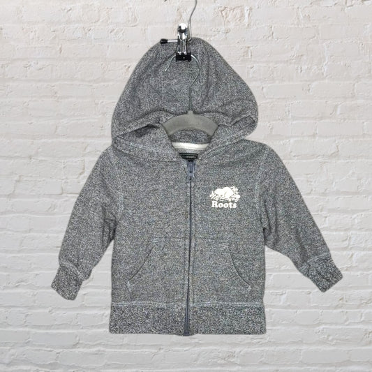 Grey Roots zip-up hoodie with logo on the chest, displayed on a hanger against a brick wall.