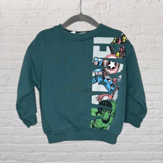 Teal Marvel Avengers sweatshirt featuring comic book characters on one side, displayed on a hanger against a white brick wall.