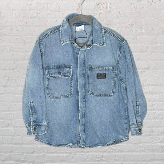Light blue denim jacket with button closure and dual front pockets, displayed on a hanger.