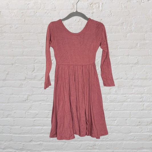 Dusty rose long sleeve midi dress with a scoop neck, hanging on a hanger against a white brick wall.