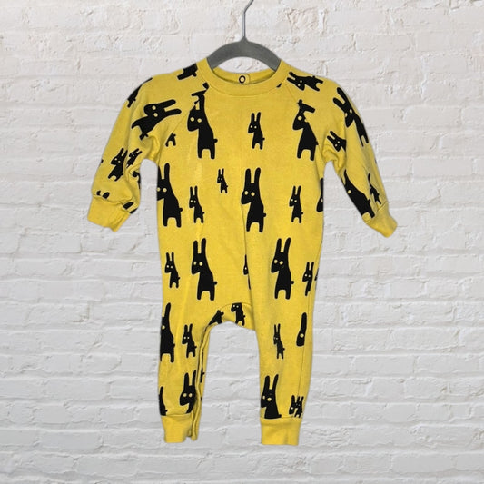 Yellow onepiece suit with black rabbit pattern for infants, displayed on a hanger against a white brick wall.