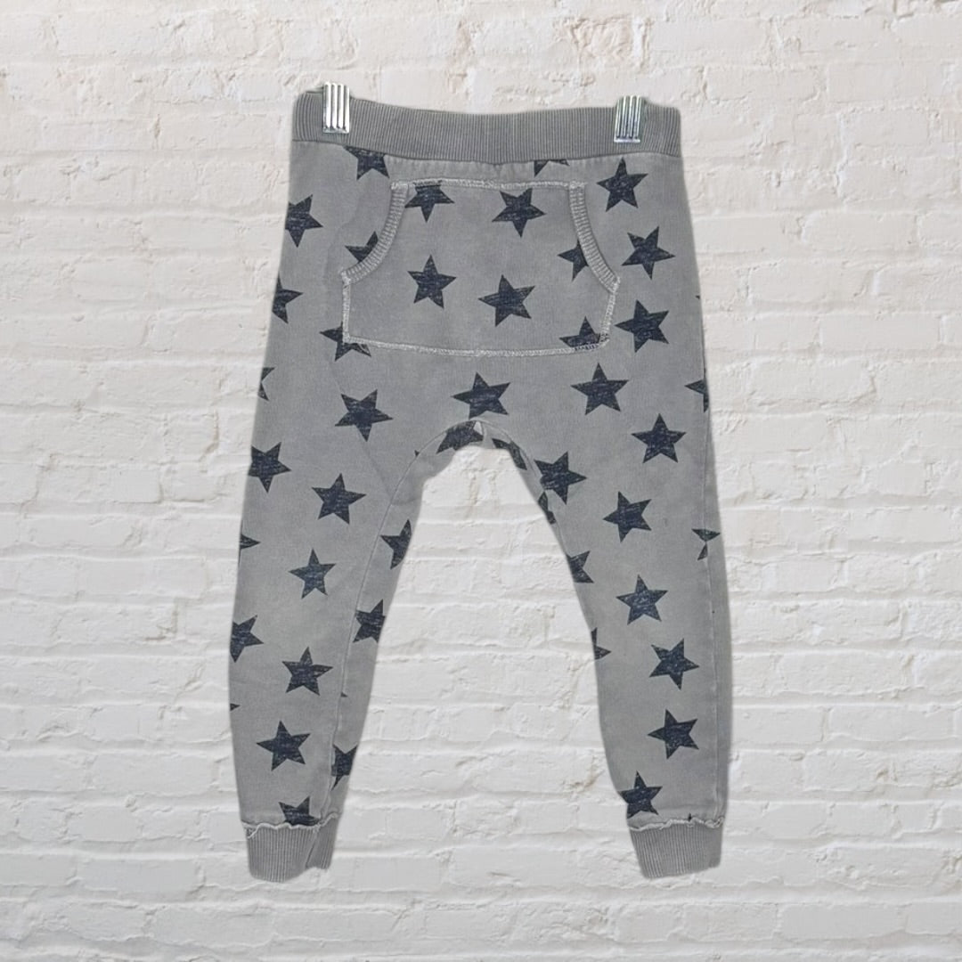 Gray jogger pants with black star print, featuring an elastic waistband and cuffs, hanging against a white brick wall.