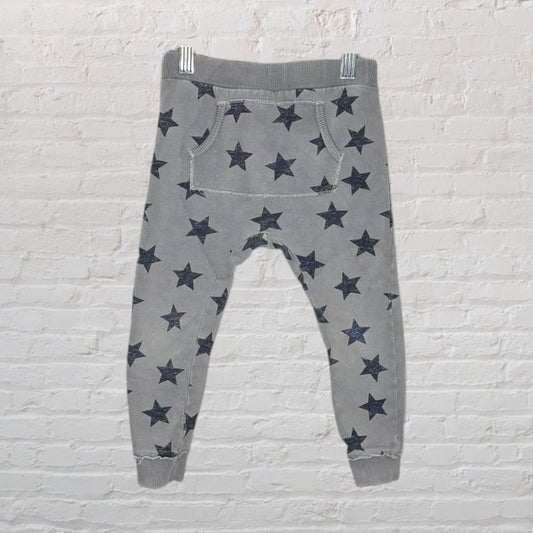 Gray jogger pants with black star print, featuring an elastic waistband and cuffs, hanging against a white brick wall.