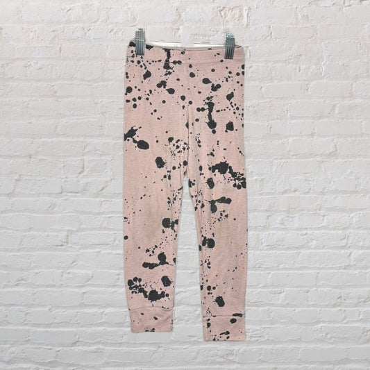 Pink leggings with black paint splatter design hanging against a white brick wall.