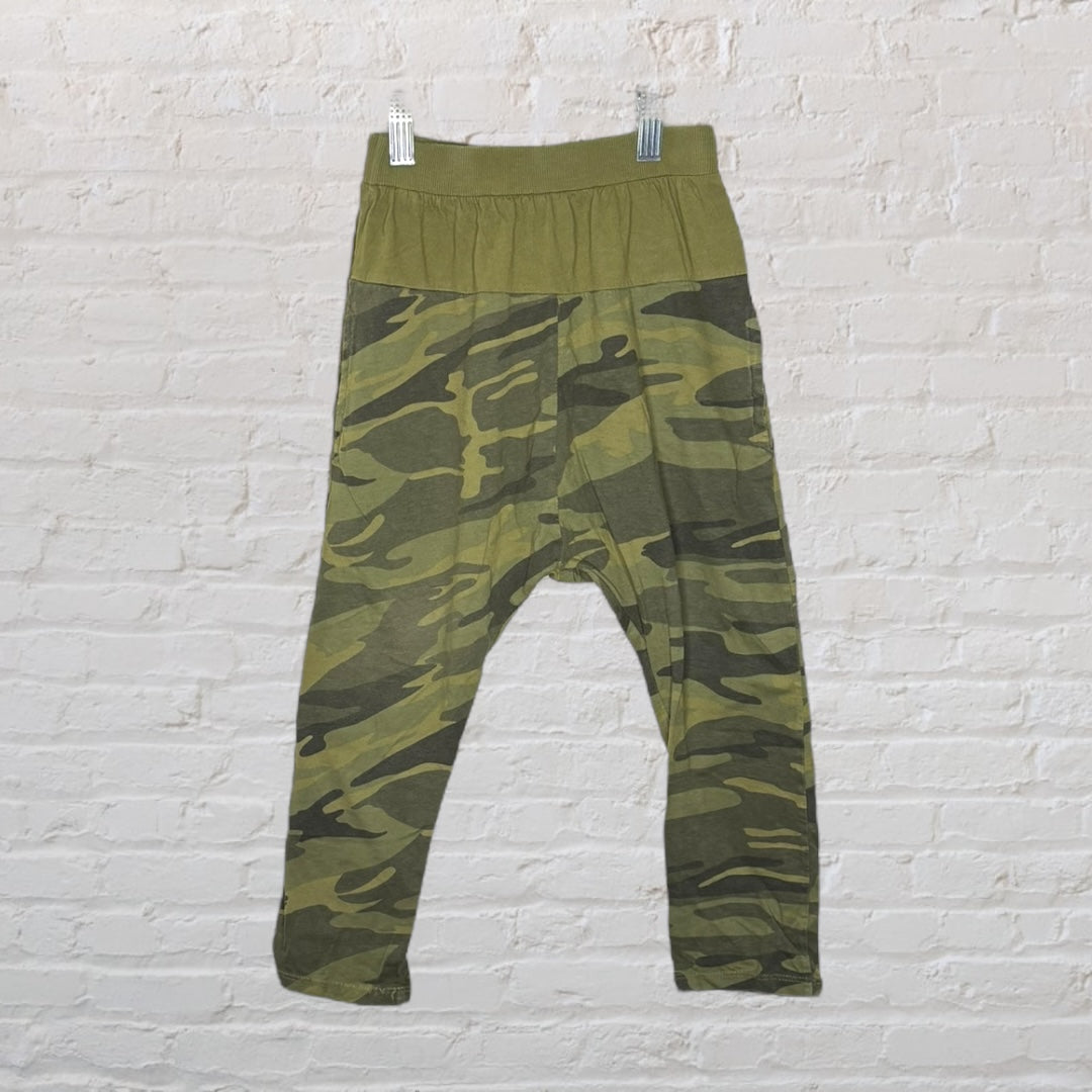 Camouflage print harem pants with a wide waistband, displayed against a white brick background.
