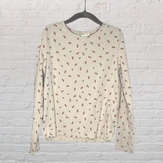 Women's beige long sleeve top with small cherry print throughout, displayed on a hanger against a brick wall.