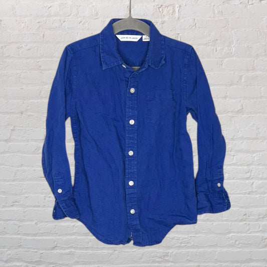Blue button-up casual shirt with a single chest pocket, by Janie and Jack, hanging against a brick wall.