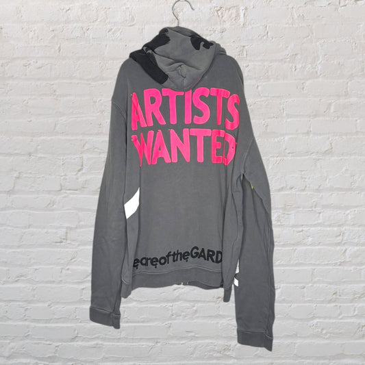 Gray hoodie with bold pink 'Artists Wanted' text and additional black text at the bottom, displayed on a hanger.