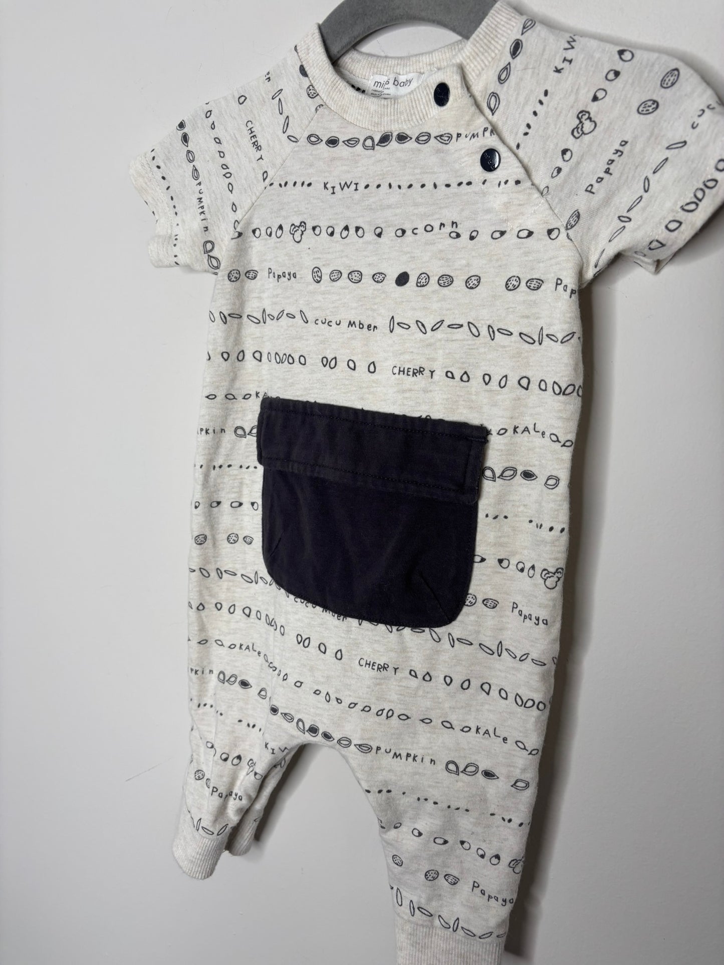 Cream-colored baby jumpsuit with black print and a large front pocket, displayed on a hanger.