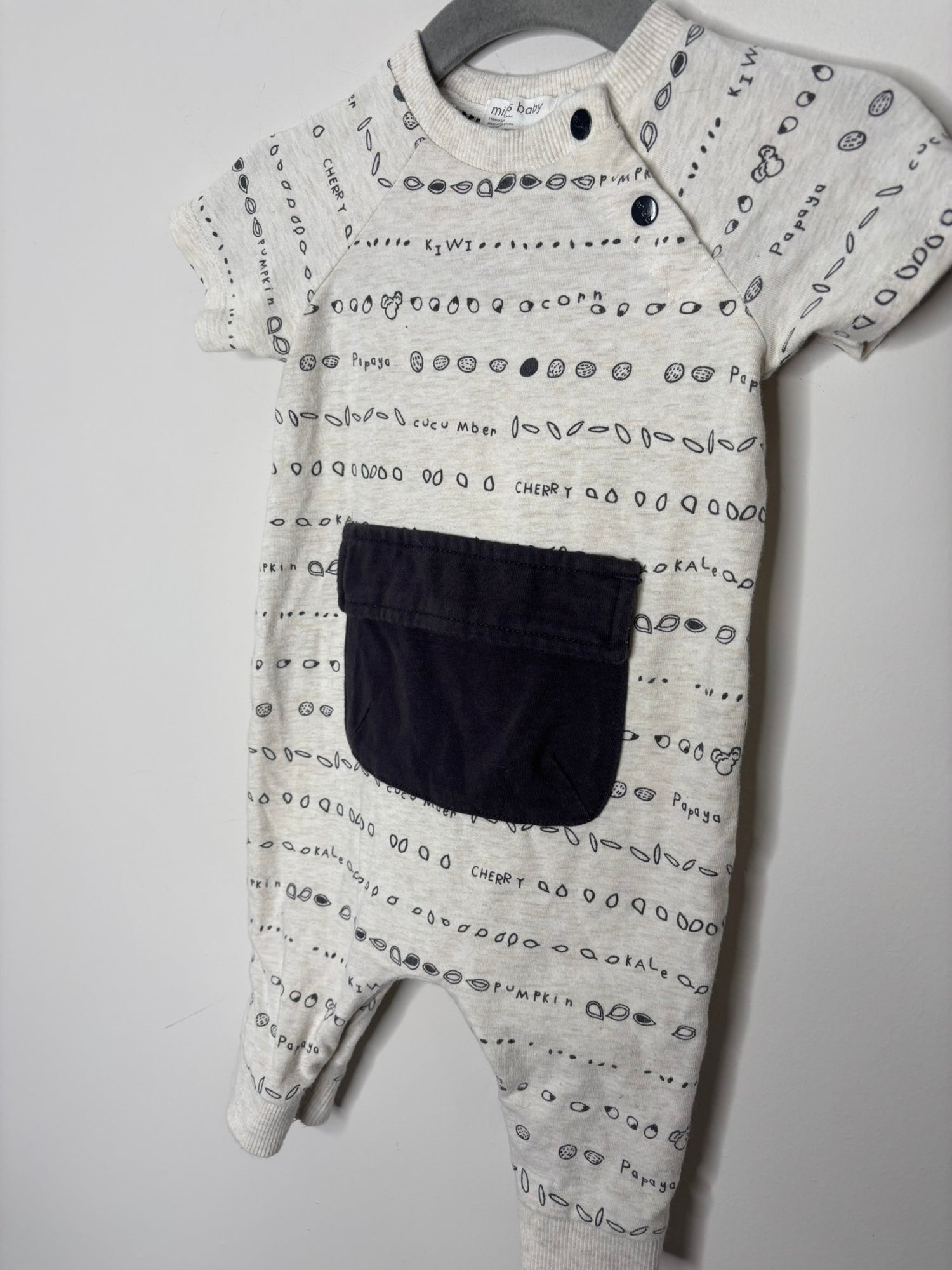 Cream-colored baby jumpsuit with black print and a large front pocket, displayed on a hanger.