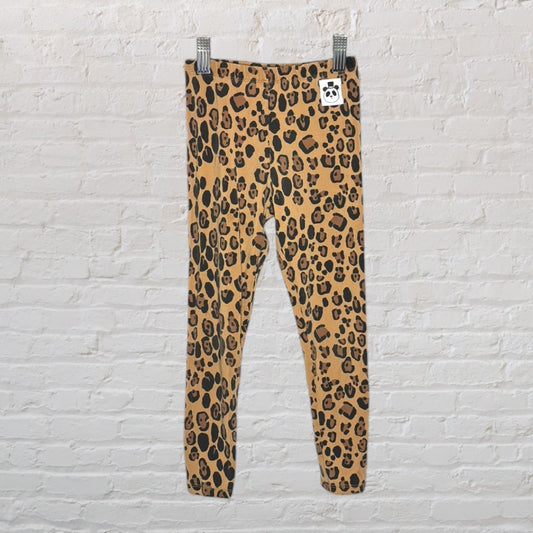 Brown and black leopard print leggings hanging on a white brick background.