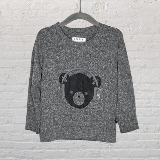 Grey Huxbaby sweatshirt with a bear wearing headphones graphic, displayed on a hanger against a brick wall.